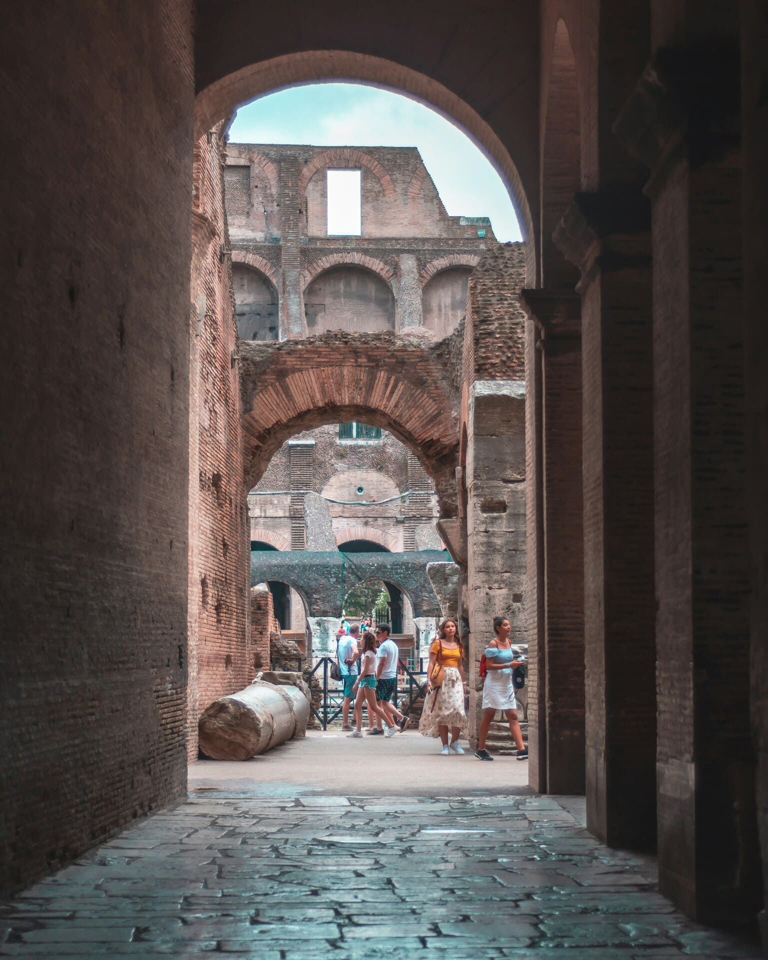 A view of an interior gallery of the Colosseum in Rome, with visitors visible in the distance.