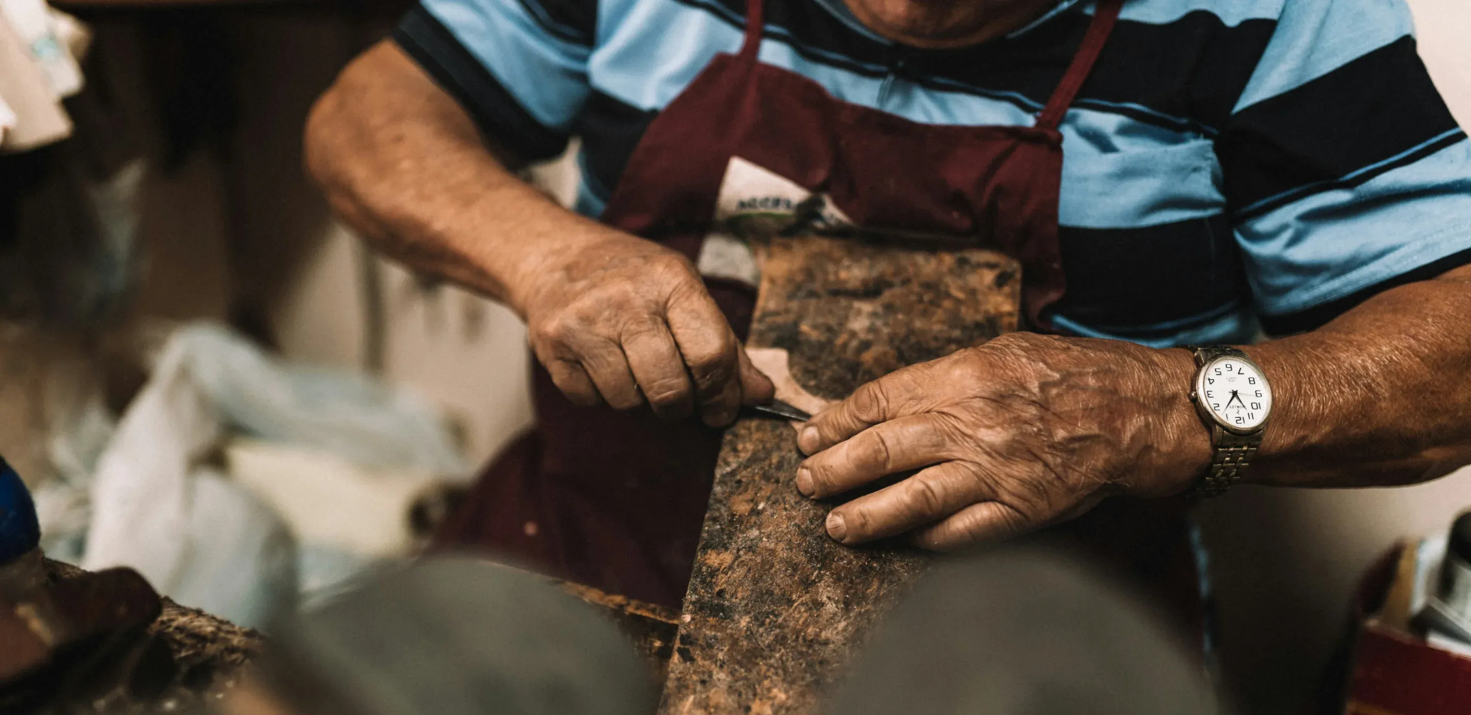 The elderly hands of an Italian craftsman are working the leather