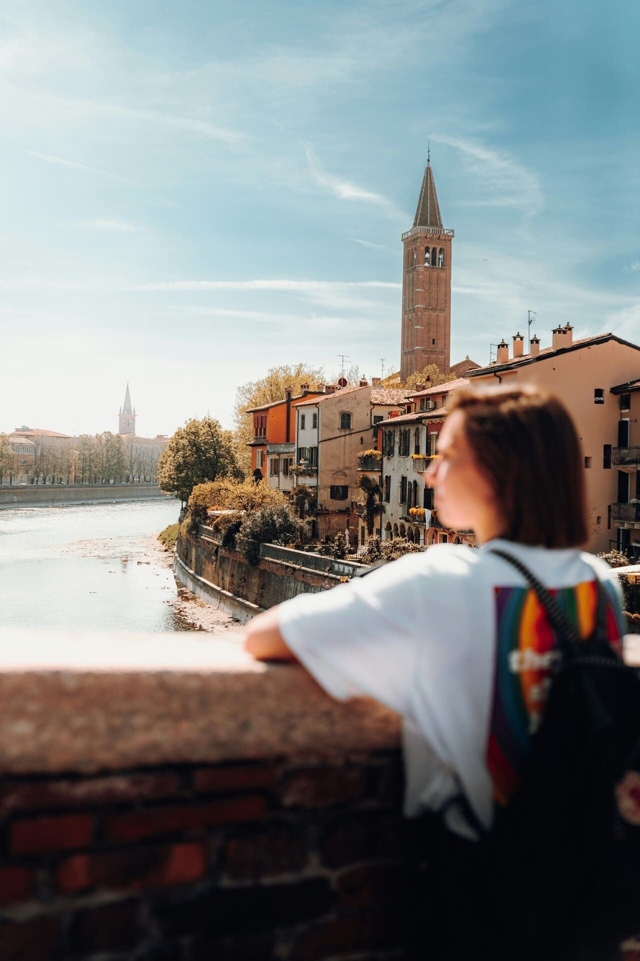 A young woman in the foreground is looking out from a bridge, with Verona visible in the background